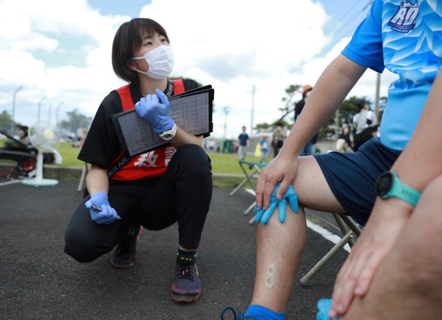 Saho Hirai, a paramedic student with the Kokushikan University Medical Team, listens to a runner explain his ailment at the first-aid station for the Kanagawa Running Association's 27th annual Friendship Half-Marathon, held April 16, 2023, in conjunction with the Hawaiian Festival on Sagami General Depot, Japan.