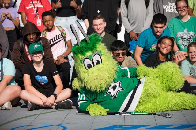 The Dallas Stars mascot, a green alien named Victor E. Green, poses with the children before they kick off the Boeing-Dallas Stars Hockey Clinic Aug. 10 on the ball hockey court. (U.S. Army photo by Blair Dupre, Fort Cavazos Public Affairs)