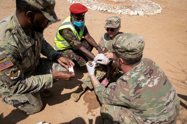 (U.S. Soldiers from the 2nd Security Force Assistance Brigade and a Kenyan Defence Force Soldier assists U.S. Army Lt. Col. Rhonda Dyer , with Civil Affairs East Africa (CA-EA), a forward deployed element of the U.S. Army Southern European Task Force, Africa (SETAF-AF), bandage a burn on a child's foot during a medical civic action program as part of Justified Accord 23 (JA23) in Larisoro, Kenya on Feb. 19, 2023.)