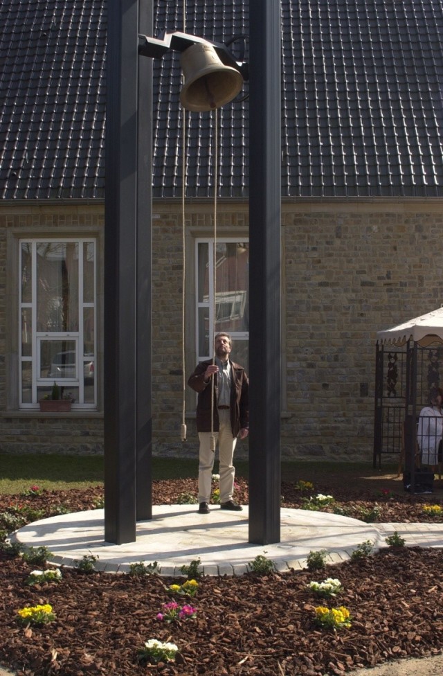 Chièvres Air Base Bell Tower: A man stands under the bell of a bell tower and pulls a rope to ring it. 