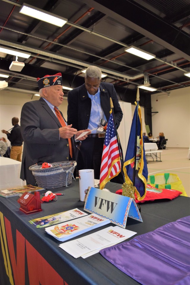 Two men stand in discussion next to a table during a retiree appreciation day event. 