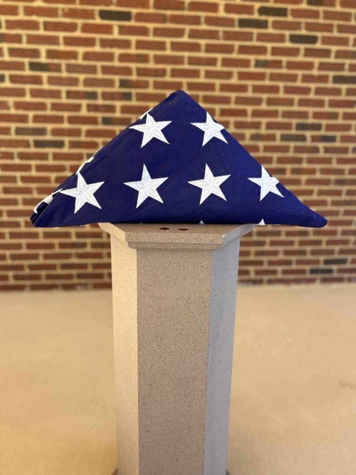 Folded American flag set atop a concrete pillar.