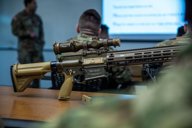 An M110A1 Squad Designated Marksman Rifle (SDMR) lays on a table in front of soldiers in class at the Pierce County Readiness Center on Camp Murray, Wash., Jan. 17, 2023.  The class is part of a training and fielding event to familiarize soldiers with new weapon systems being introduced to the 81st Stryker Brigade Combat Team and 96th Troop Command.