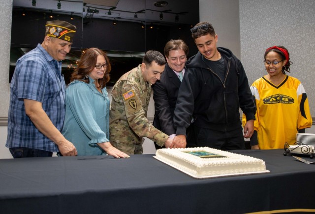 Command Sgt. Maj. David A. Rio, center, senior enlisted leader of U.S. Army Garrison Japan, and other community members cut a cake to help kick off this year's Army Emergency Relief campaign at the Camp Zama Community Club in Japan, March 2, 2024. About 200 people attended the event, which also had a modeling fair to help spread the word about the campaign.
