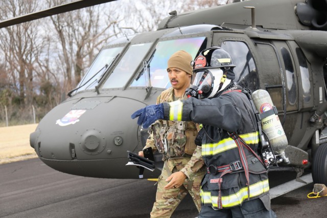 A U.S. Army Garrison Japan firefighter escorts one of the UH-60 Black Hawk helicopter pilots to safety during a downed aircraft exercise at Camp Zama, Japan, March 7, 2024. The firefighters arrived at the scene within two minutes while using radio communication to coordinate their efforts with the air traffic control tower.