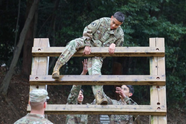 Cadet Ian Leon Quinones, top, climbs an obstacle with help from Cadets Thomas Diaz and Noah Hogan as part of a confidence course at Camp Zama, Japan, March 12, 2024. Soldiers from the 35th Combat Sustainment Support Battalion hosted a field day to familiarize Zama Middle High School cadets with some aspects of Army life.