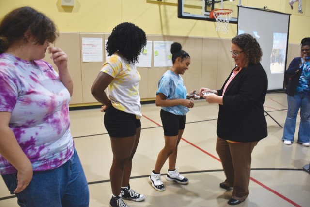 Greta Buccellato, Fort Cavazos deputy to the garrison commander, presents teens Malia O'Neal, Leele Fitzpatrick and Gem Jenkins with challenge coins following the Teen Chain Communication forum March 14, 2024, at Montague Youth Center. (U.S. Army photo by Janecze Wright, Fort Cavazos Public Affairs)