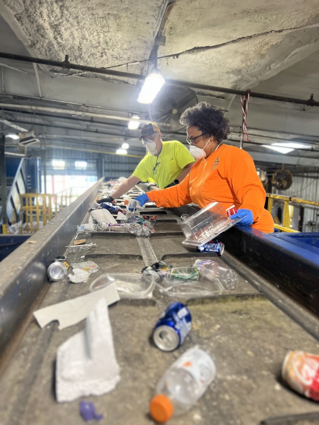 Two people sort through recycled items on a conveyor belt. 