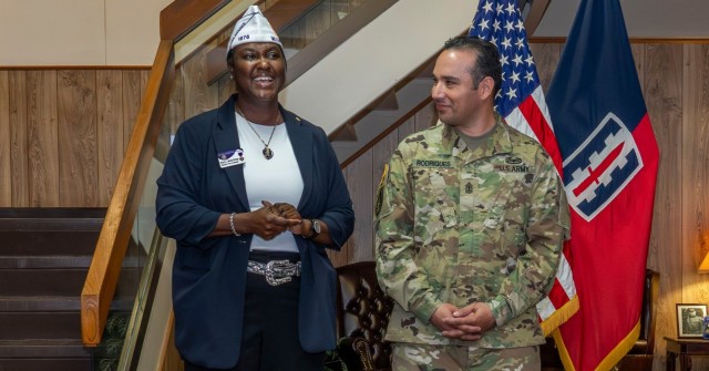 Two people, a woman on the left and a man on the right, stand while the woman speaks and the man looks on. 