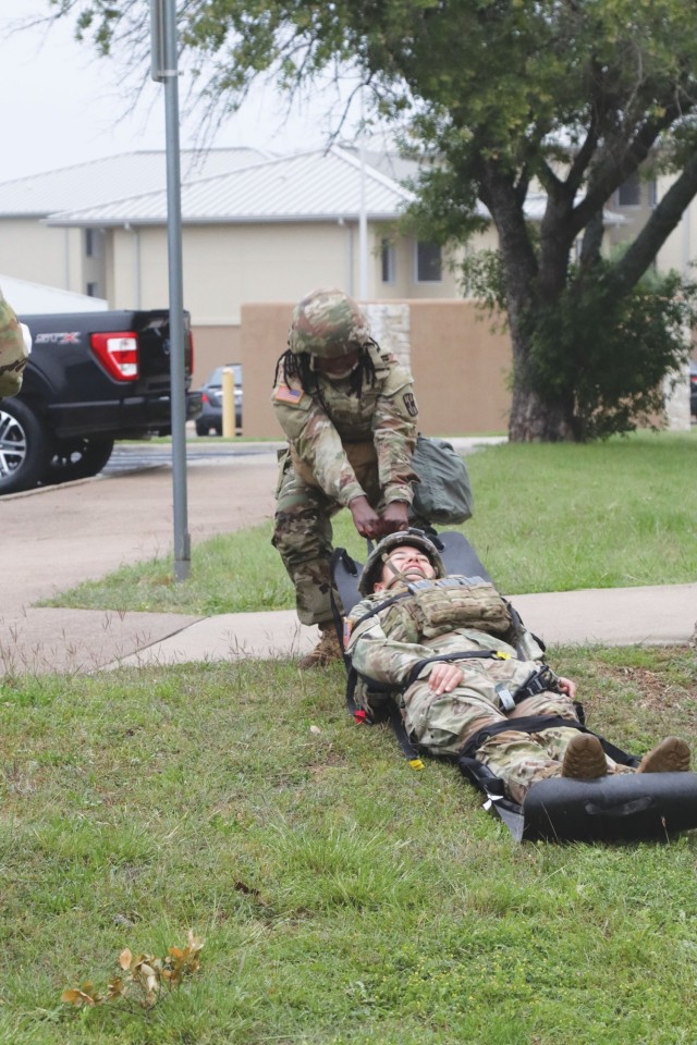 A woman in an operational camouflage pattern, or OCP, uniform drags another woman, also in OCPs, on a black mat outside. 