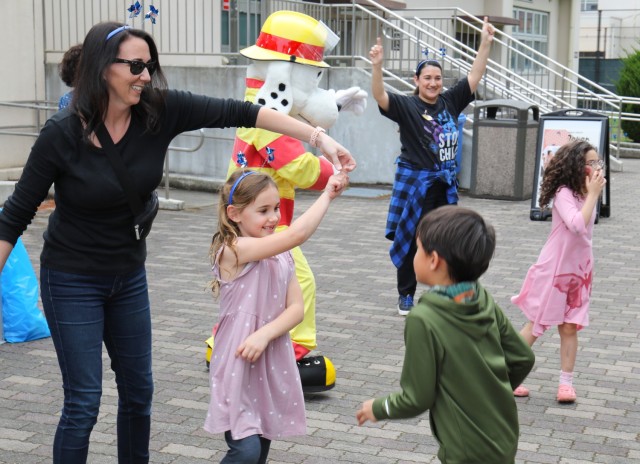 Community members dance with Sparky, the fire department's mascot, during a pinwheel planting event in support of National Child Abuse Prevention Month April 30, 2024.