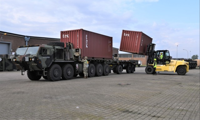 A forklift loads metal containers onto a military vehicle.