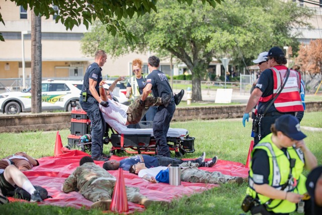 Five people lay on a tarp while two people work together to lift up another person, one grabbing the by the armpits while the other grabs the legs. 