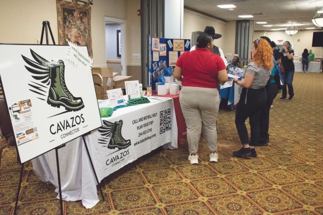 A board sitting on a stand holder that reads "Cavazos Connector" stands beside a covered table with infographics and free goodies. 