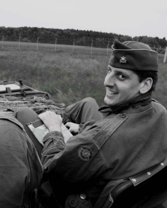 A black and white photo of a man dressed in a WWII uniform riding in a jeep.