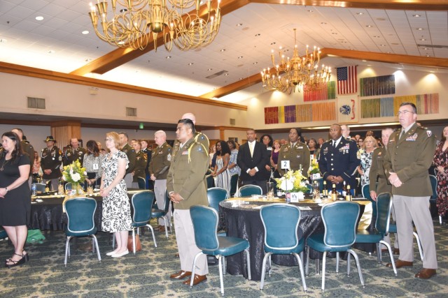 A crowd of people stand at a ballroom around the tables.