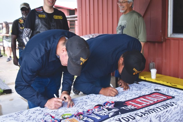 Two men bend down over a table with a large cloth banner on it, writing on it with permanent markers. 