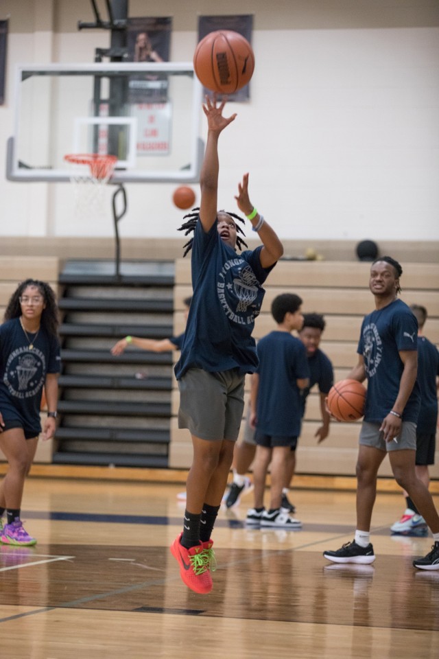 A kid jumps up as he releases a basketball in the air while on a basketball court.