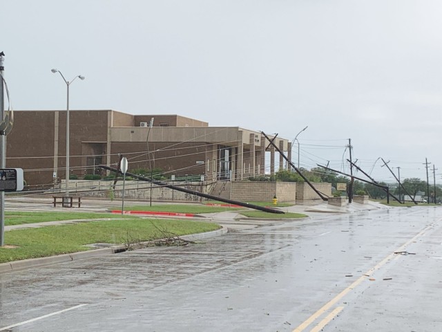 A row of electrical poles along the left side of a wet street lay at different angles away from the street.