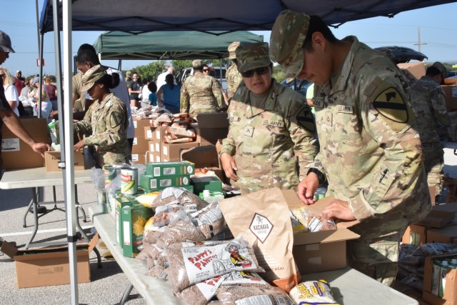 Two people in operational combat pattern uniforms look down at a table full of bagged and boxed food.