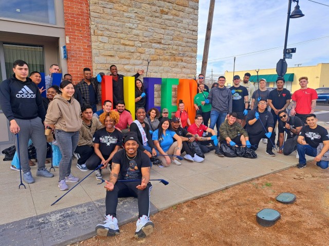 A group of people pose for a picture in front of a building, crowding around a sign that reads, "Killeen."