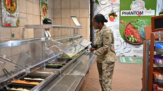 A woman stands at a bar filled with tubs of different foods, looking at them.