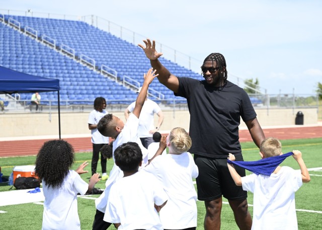 A man holds his right hand up in the air as a young boy jumps up, his right hand stretching to meet the man's, as four other children around him look on.