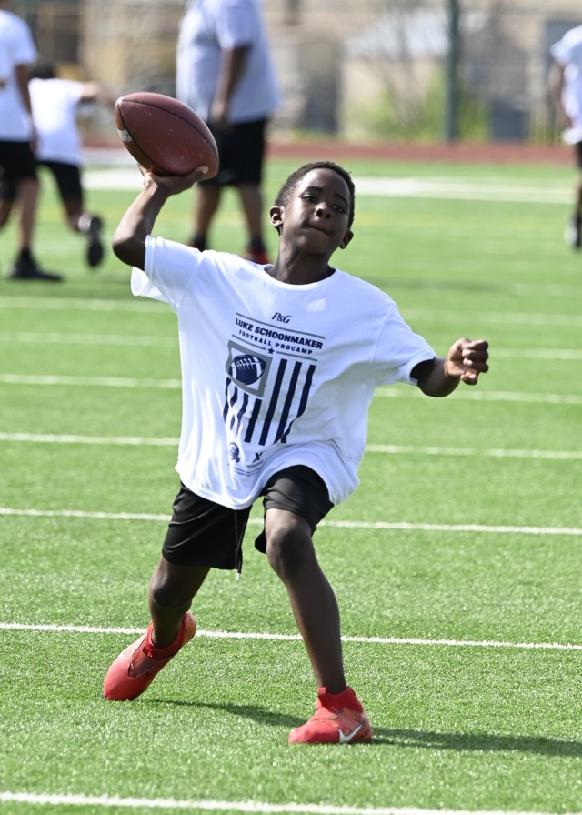 A young boy prepares to throw a football, right hand angled back with the football in hand and left foot forward.