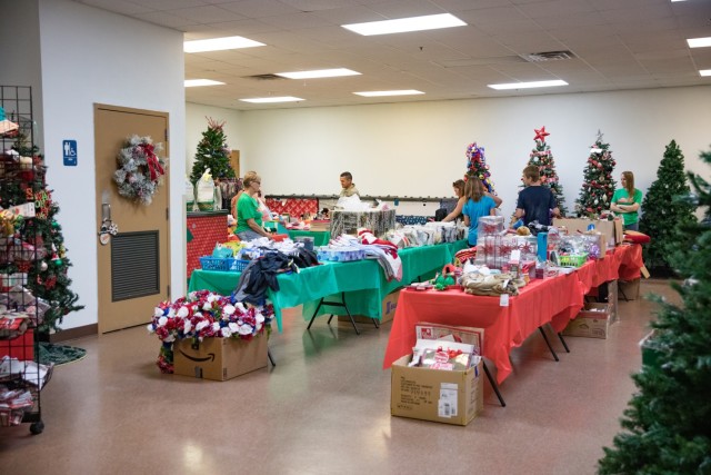 People standing mill around tables piled with various items, including holiday decorations.