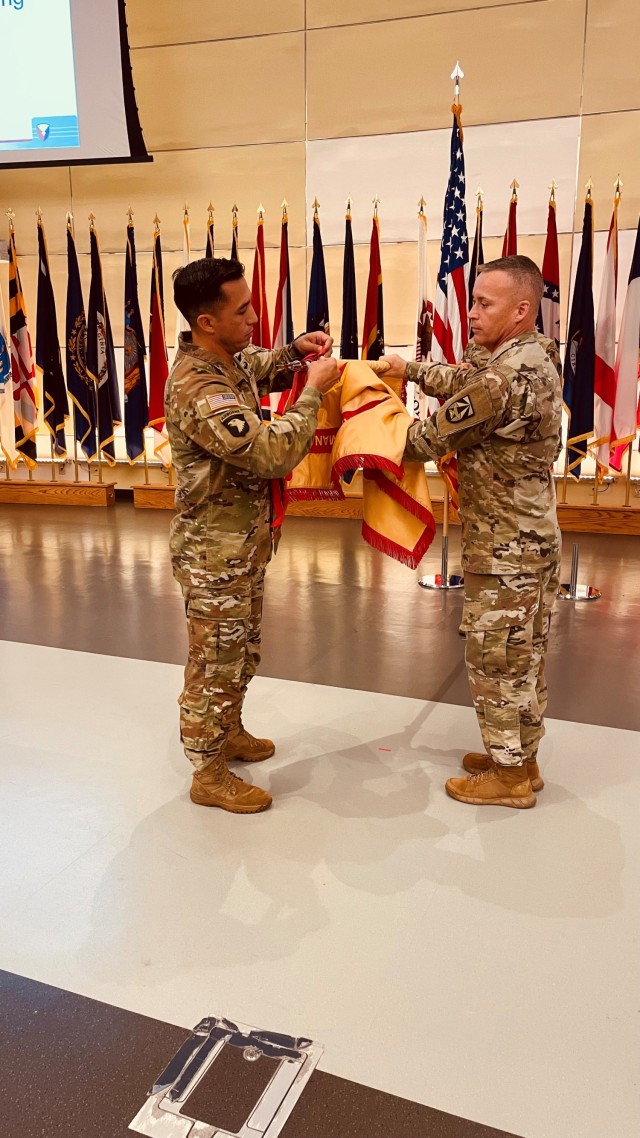 FORT DETRICK, MARYLAND - Fort Detrick Garrison Commander Col. Christopher Chung and Garrison Command Sgt. Maj. Michael Dills hang the Army Superior Unit Award streamer to the Installation Management Command flag during a townhall in the auditorium...
