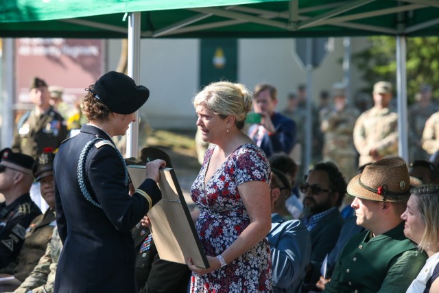 USAG BAVARIA - HOHENFELS, Germany -- Capt. Katrina Josberger, commander of Bravo Company (Blackfoot), 1st Battalion, 4th Infantry Regiment, presents a plaque with a replica of a street sign to Rachel Heiner, sister of fallen B Co. commander Capt....