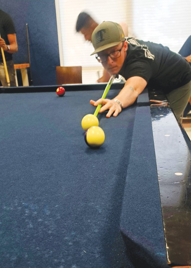 A man stretches his left army along the pool table, holding a pool cue and aiming for a yellow ball.