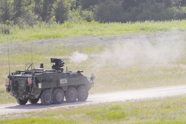 A Nuclear, Biological, and Chemical Reconnaissance Vehicle, or NBCRV, fires from a gun attached to the top from a dirt road in an open grass field.