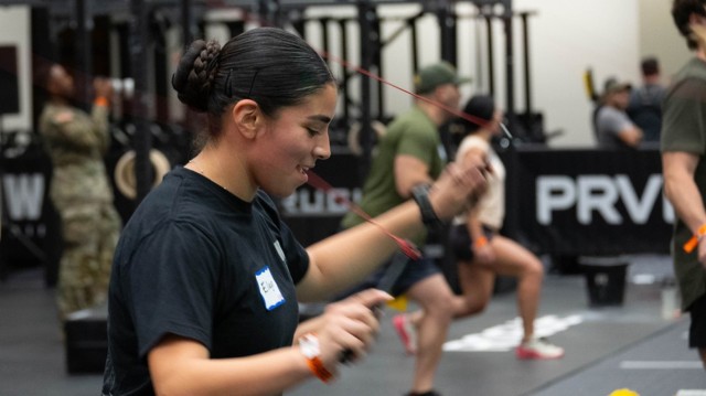 A woman swings a jump rope while wearing a black T-shirt and hair pulled back in a braided bun.