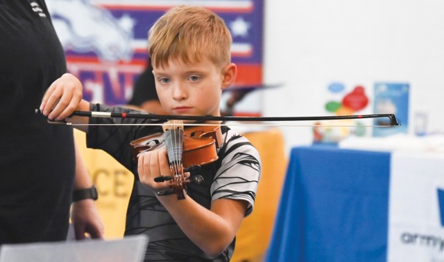 A boy holds a bow perpendicular to a violin resting underneath his chin.