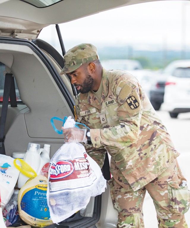 A man dressed in an Army combat uniform moves a plastic bag into an open car trunk.