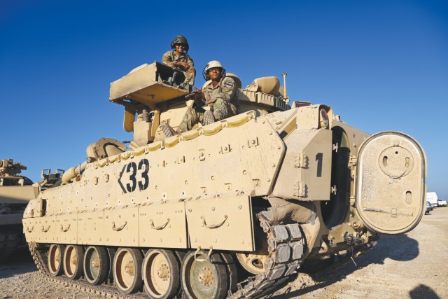 Two men dressed in Army combat uniforms pose for a picture atop a M2A2 Bradley, a military fighting vehicle.