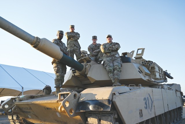 Four men dressed in Army combat uniforms pose for a photo atop an M1A2 Abrams tank.