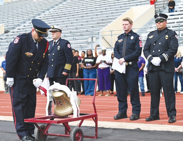 A man bends down slightly, ringing a bell attached to a cart as others standing to the left of him look on.