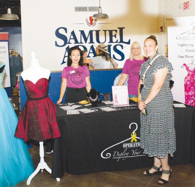 Three women standing around a table covered in a black tablecloth pose for a photo, smiling.