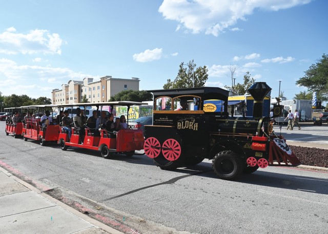A vehicle decorated like a steam train with carts full of people sitting on them attached sits on a road.