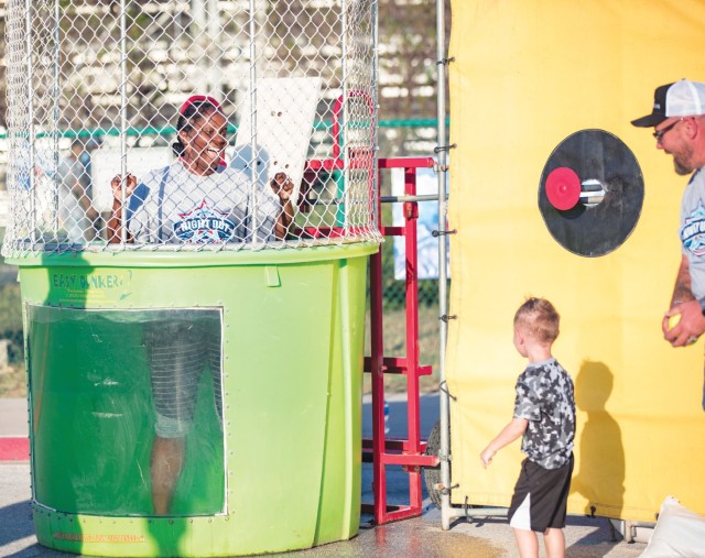 A woman stands in a filled dunking tank as a child and man look on.