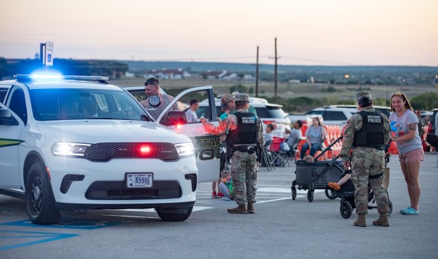 People interact with military police officers and check out a police cruiser in a parking lot.