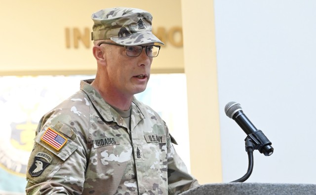 A man dressed in an Army combat pattern uniform speaks behind a podium with a microphone.