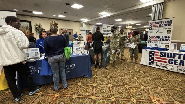 People stand and walk past clothed-covered tables covered in freebies and infographics.