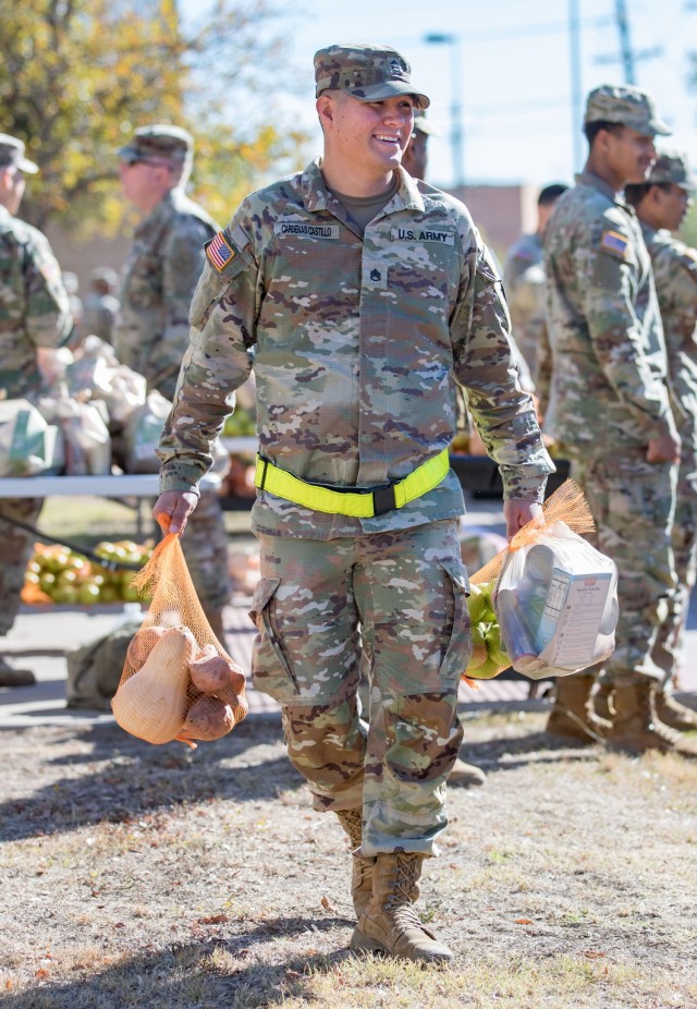 A man standing and dressed in an Army combat pattern uniform holds bag of food in both hands.