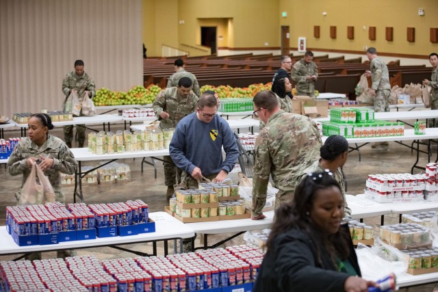 People standing behinds row of tables filled with packaged foods pack the foods into plastic bags.