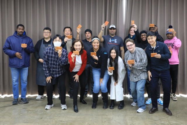 A group of 15 U.S. Soldiers, KATUSAs, and civilians assigned to U.S. Army Garrison Yongsan-Casey and 210th Field Artillery Brigade take a commemorative photo after saddle stitching leather wallets during a Newcomers Cultural Awareness and...