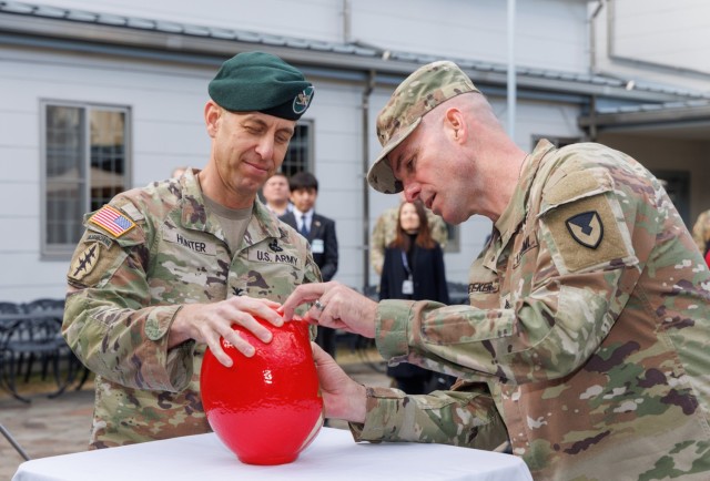 Col. Marcus Hunter, left, commander of U.S. Army Garrison Japan, watches Command Sgt. Maj. Rick Meeker, right, paint in one of the eyes of a "daruma" doll during a ceremony at Camp Zama, Japan, Dec. 12, 2024. Meeker assumed responsibility...