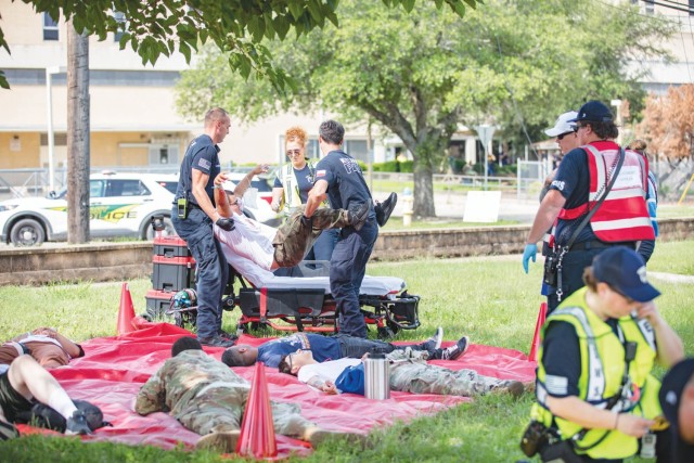 Five people lay on a tarp while two people work together to lift up a man, one grabbing him by the armpits while the other grabs the legs.